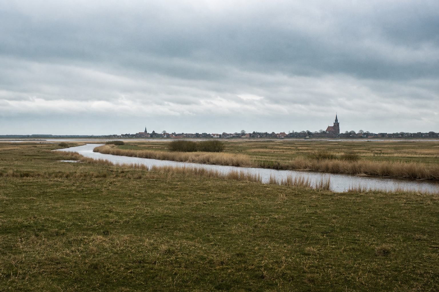 Panorama norddeutscher Wiesen, Wasser und ferner Siedlung